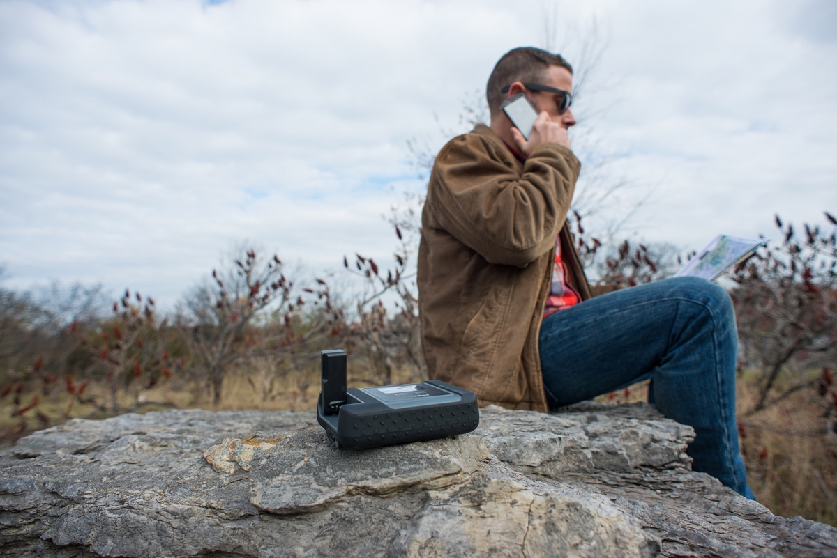 Iridium GO! on a rock while a man beside it makes a call on his smartphone